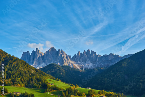 Amazing autumn scenery in Santa Maddalena village with church, colorful trees and meadows under rising sun rays. Dolomite Alps, Italy.