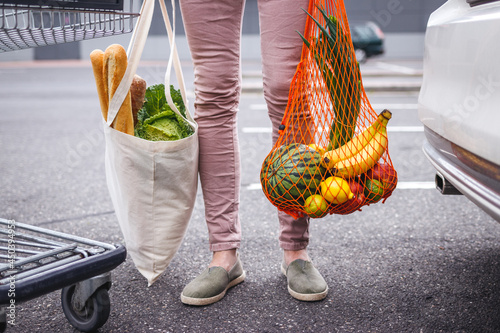 Reusable textile shopping bag and mesh bag with groceries purchased. Woman standing at parking lot after shopping at supermarket. Ethical consumerism and sustainable lifestyle with zero waste photo