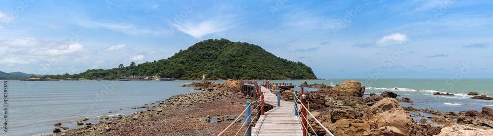 wide panorama view of seascape wooden bridge with rope rail to white pagoda on rock in blue sea, big mountain, and blue sky with cloud, Chedi Ban Hua Laem, travel destination in Chanthaburi, Thailand.