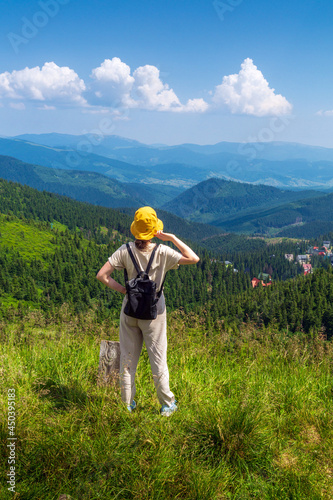 The traveler in hat and backpack resting in nature. A tourist girl looks at the panorama of the mountains. Mountain beautiful landscape