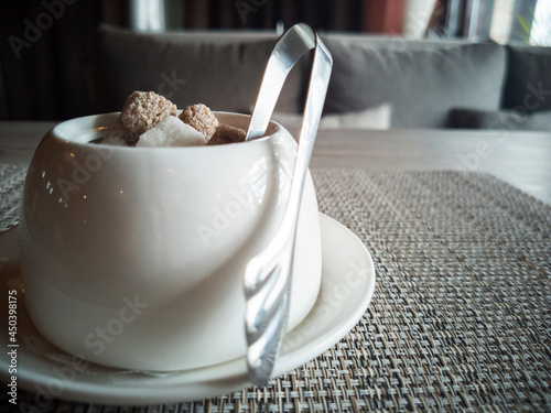 White deep glass bowl with white and dark sugar lumps and metal tweezers on gray backing photo