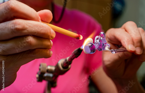 Hands of the glassmaker  making figurines from glass. Shaping hot Murano glass into a bunny under a jet of fire from a gas burner. Handmade fine art. Selective focus. Close up.
