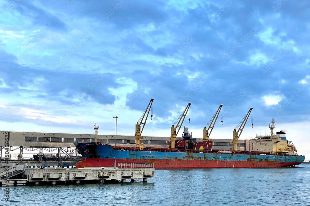 View from the water on the Bulk cargo ship under port crane bridge. Dry cargo terminal with cargo ship. Sea ship