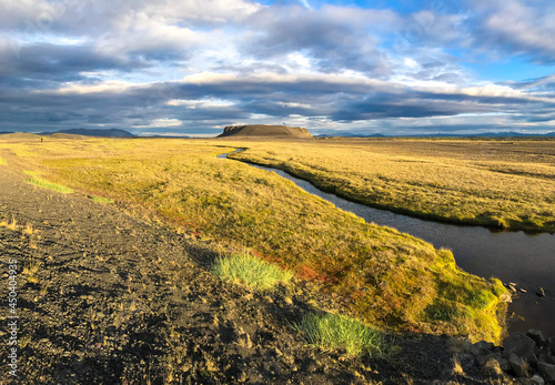 Panorama at river flows among orange dry grass field to mountain in Iceland 