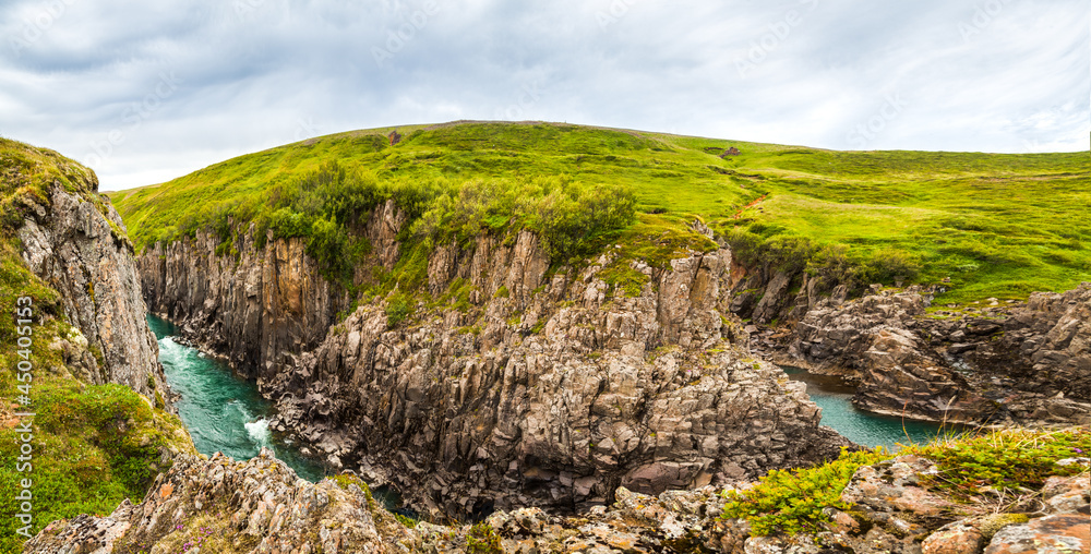 Green Icelandic Tundra. Fast river with glacial water flows among cliffs canyon 