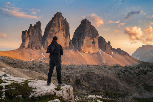 Three peaks of Tre Cime di Lavaredo during sunset and male standing from behind in foreground