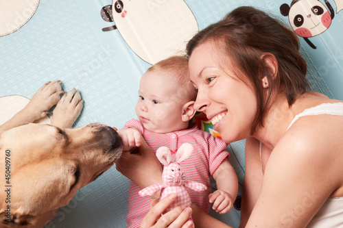  Happy young mother laying in bed with a dog and newborn baby daughter. View from the top.