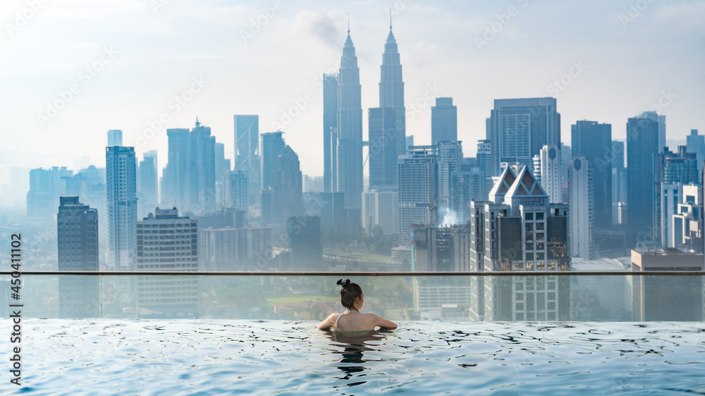 Naklejka premium Asian travel concept. young woman enjoying with the city sky view from hotel roof top swimming pool, beautiful girl lifestyle outdoor in vacation time