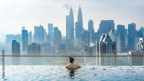 Asian travel concept. young woman enjoying with the city sky view from hotel roof top swimming pool, beautiful girl lifestyle outdoor in vacation time