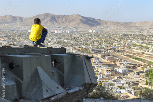 Boy sitting on Destroyed Tank on the hills over Kabul City in Afghanistan photo