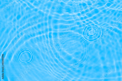 Surface of light deep blue transparent swimming pool water texture with circles on the water. Trendy abstract nature background. Water waves in sun light reflections