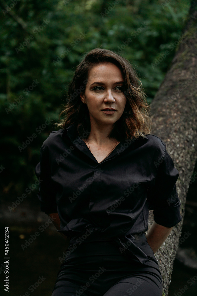 Young woman - close portrait in a dark pine forest. Woman in black shirt