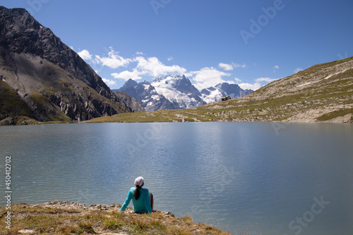 Woman Sitting at the edge of Lac du Gol  on in the French Alps with the Mountain Peak La Grave in the Distance