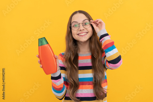 cheerful child long hair in glasses presenting shampoo bottle, advertisement