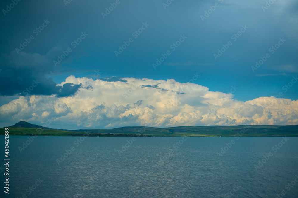 The opposite shore of the azure lake against the blue sky with white clouds.