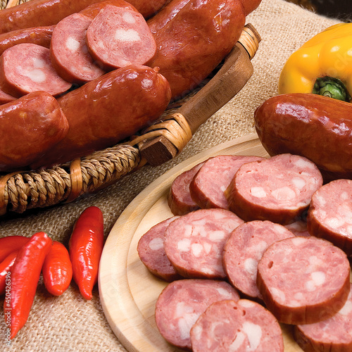 Produção de linguiça calabresa fatiada em tábua de madeira e cesta de vime, decorada com pimenta vermelha e pimentão amarelo, sobre toalha de juta. photo
