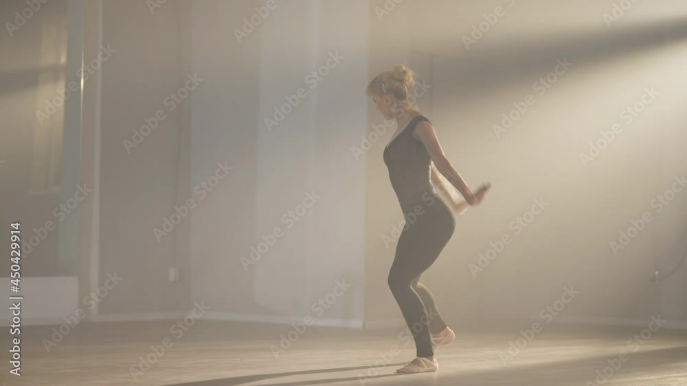 Wide shot of dancing ballerina in backlit fog indoors. Slim confident professional Caucasian female ballet dancer rehearsing in front of mirror in dance studio. Slow motion Wide shot of dancing ballerina in backlit fog indoors. Slim confident professional Caucasian female ballet dancer rehearsing in front of mirror in dance studio. Slow motion