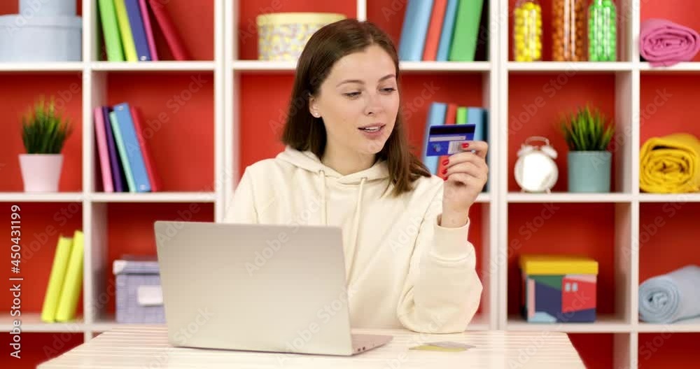 Happy female shopper using instant easy mobile payments making purchase in online store. Smiling young woman customer holding credit card and laptops sitting at the table at home.
