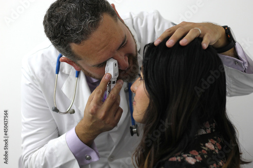 Doctor examining his latin woman patient checking ear, eyes and body reflexes, regular examination 