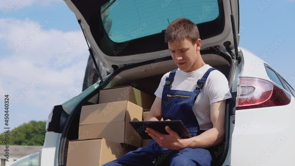 The courier sits on the edge of the open trunk, filled with boxes of goods and fills out documents. Delivery of goods home The courier sits on the edge of the open trunk, filled with boxes of goods and fills out documents. Delivery of goods home