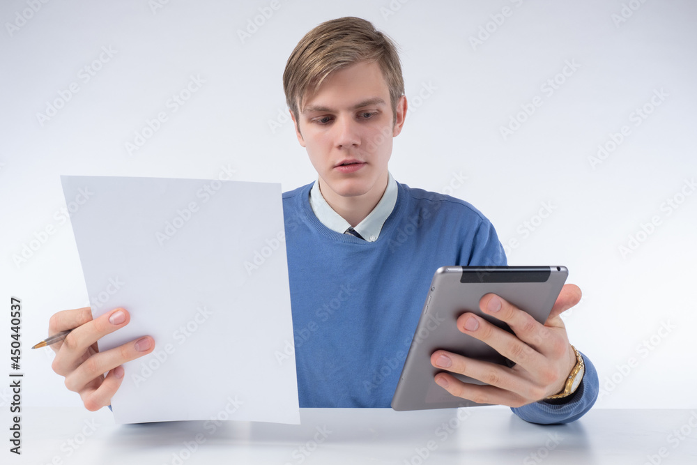 Online training. A young man with a sheet of paper and a tablet computer in his hands. Search for information on the Internet. Using gadgets at work and at school. Training on online courses.
Online training. A young man with a sheet of paper and a tablet computer in his hands. Search for information on the Internet. Using gadgets at work and at school. Training on online courses.