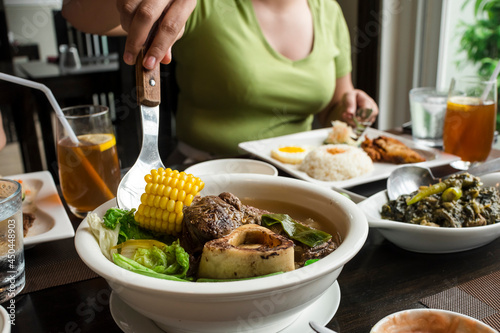 An anonymous woman scoops a piece of corn from a bowl of Beef Bulalo. At a Filipino cuisine restaurant. photo