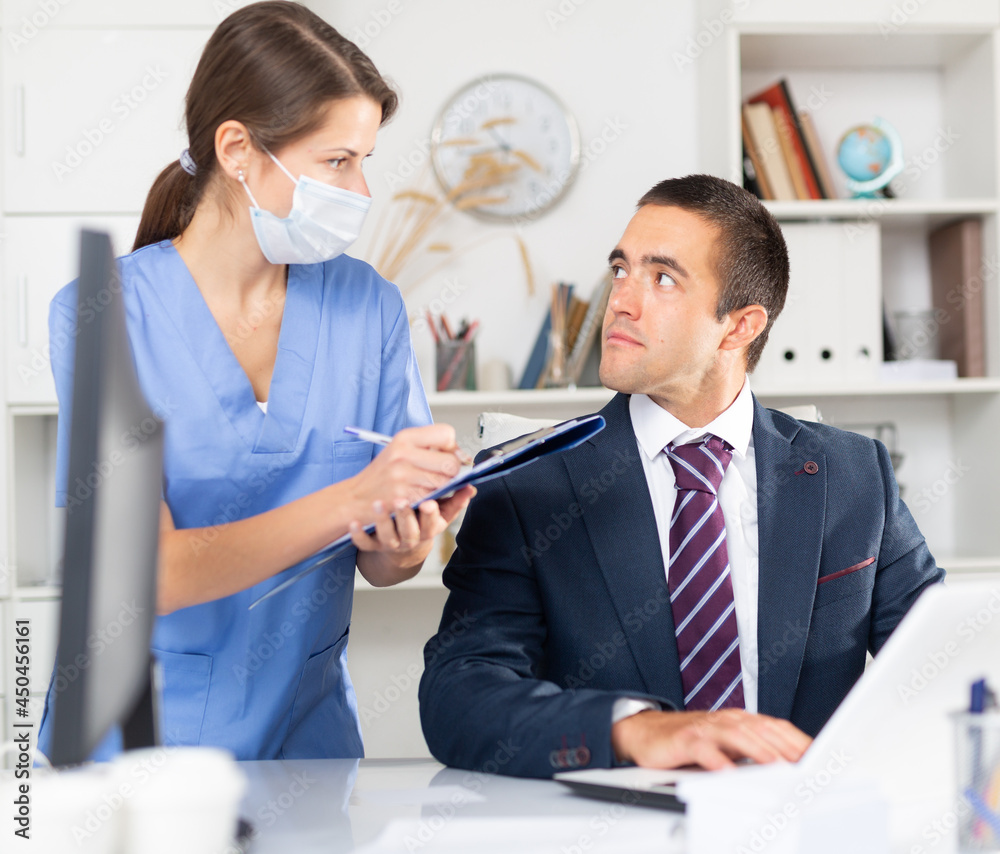 Fototapeta premium Young woman professional medical worker monitoring state of health of businessman working in office. Pandemic precautionary concept