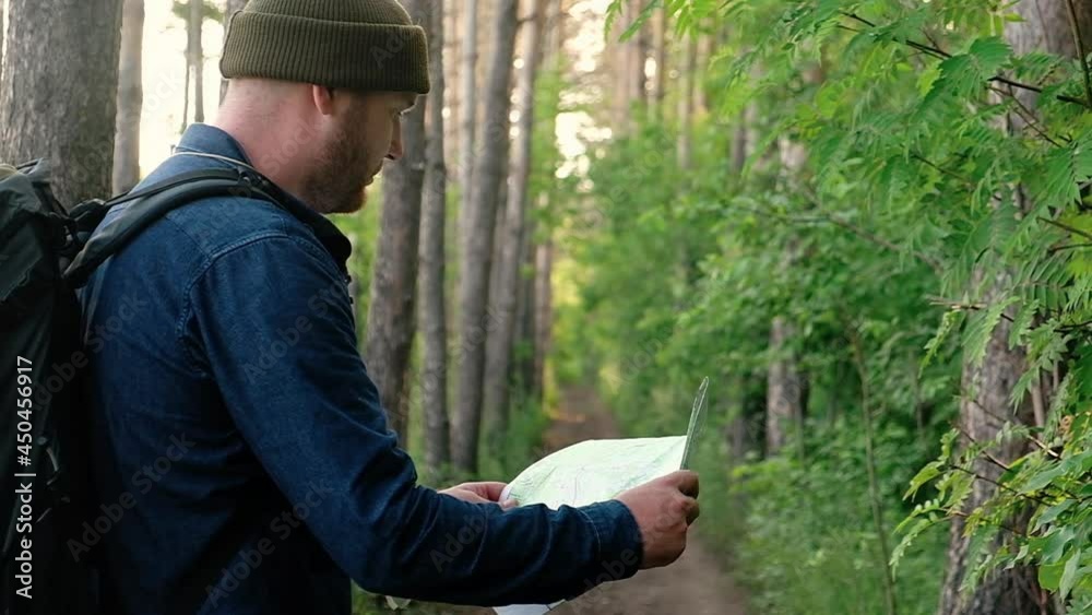 Man is traveling on foot along forest paths. tourist in forest holds paper map in his hands to navigate terrain in search of way out. Active weekend outside with backpack. traveler uses map of area Man is traveling on foot along forest paths. tourist in forest holds paper map in his hands to navigate terrain in search of way out. Active weekend outside with backpack. traveler uses map of area