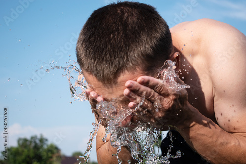 young white man washing his face with water on a blue sky background