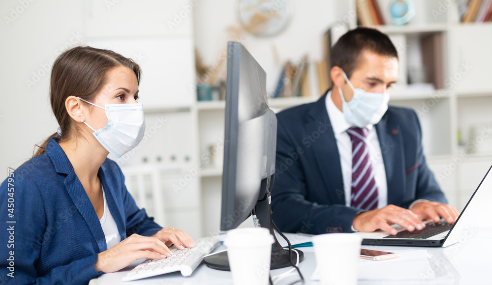Fototapeta premium Portrait of young business woman focused on work with male colleague in office. People wearing medical face masks to prevent spread of viral infection