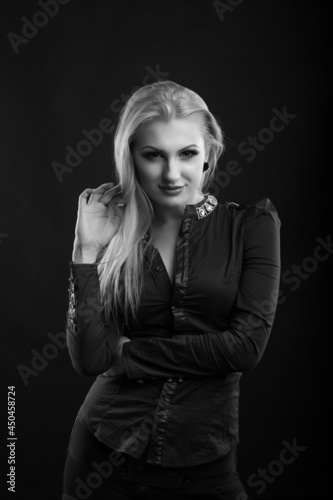 Wonderful blond lady with perfect makeup and long straight hair wears blouse, posing at studio. Black and white sho
