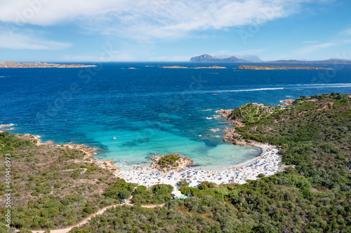 View from above, stunning aerial view of a white sand beach full of beach umbrellas and people swimming in a turquoise water. Spiaggia del Principe,Sardinia, Italy.