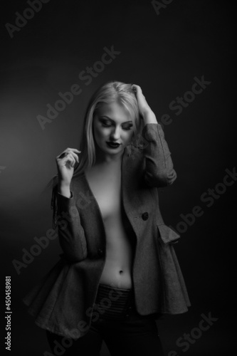 Tender blond woman with bright makeup and long hair wears jacket on a naked body