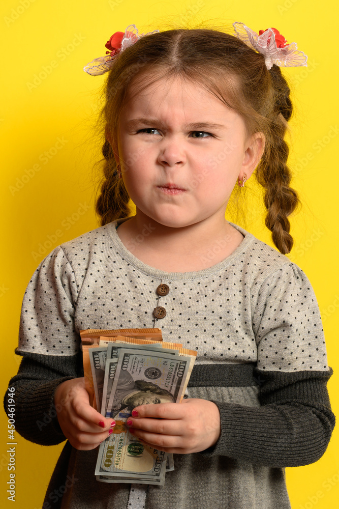 Cute little girl on a yellow background background holds the world's currency, financial literacy and development in children. Cute little girl on a yellow background background holds the world's currency, financial literacy and development in children.
