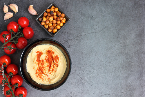A bowl for homemade hummus, decorated with boiled chickpeas, paprika on a dark concrete background. the concept of a healthy vegatarian diet. cherry and garlic Top view.