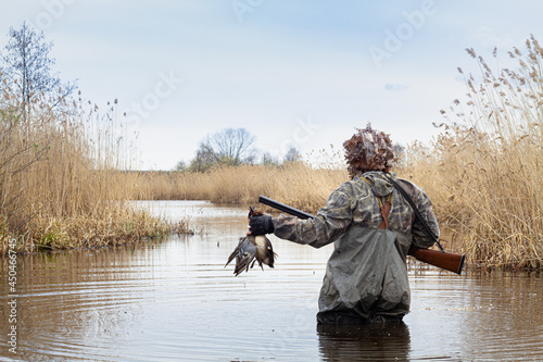 the hunter is standing in the lake with two shot ducks in his hands photo