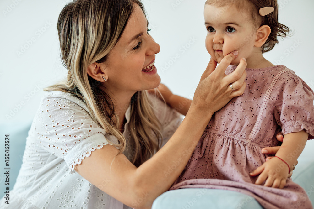Young beautiful mother sitting at home with her baby girl and stiffing its chubby cheeks. Young beautiful mother sitting at home with her baby girl and stiffing its chubby cheeks.
