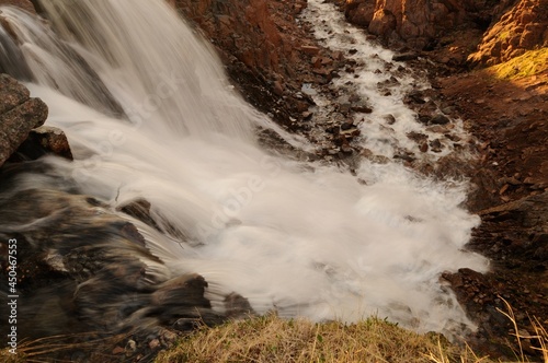 Mountain river, water descends from the mountains over the stones and falls to the bottom .. Freshwater waterfall descends from the mountain in the photo with a long exposure.