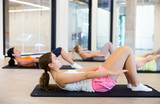 Positive young woman doing exercises during group training in modern yoga studio indoor