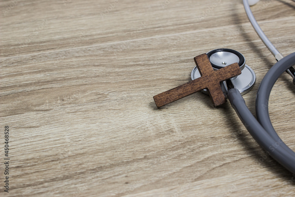 A stethoscope with wooden cross on a wooden table. A stethoscope with wooden cross on a wooden table.