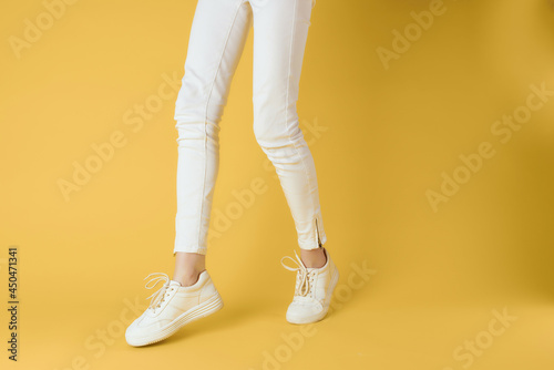 female legs in white pants sneakers fashion yellow background