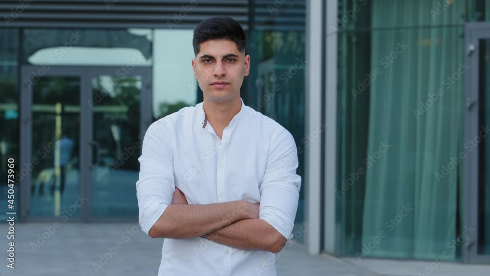 Close-up headshot confident serious concentrated Indian Arabic young man wearing shirt stand posing with arms crossed, looking at camera portrait. Thoughtful millennial guy student or businessman