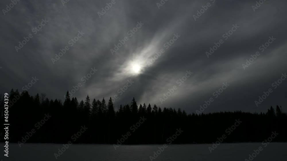 Time lapse of mystical sunrise behind thin cloud sheet on icy lake scenery. Silhouette of spruce trees in the background. Time lapse of mystical sunrise behind thin cloud sheet on icy lake scenery. Silhouette of spruce trees in the background.