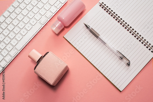 Business concept. Workspace with business accessories and female cosmetics: keyboard, pen, notebook, perfume and dry flowers on a pink background 