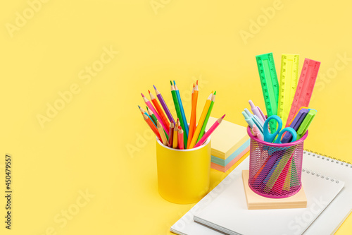 Two glasses with pencils, pens, markers, scissors and rulers stand on a yellow background on a notepad. A place to copy. Advertising, design, perfect retouching.