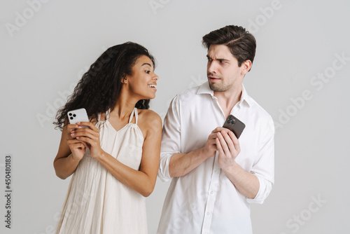 Young multiracial couple frowning while using mobile phones