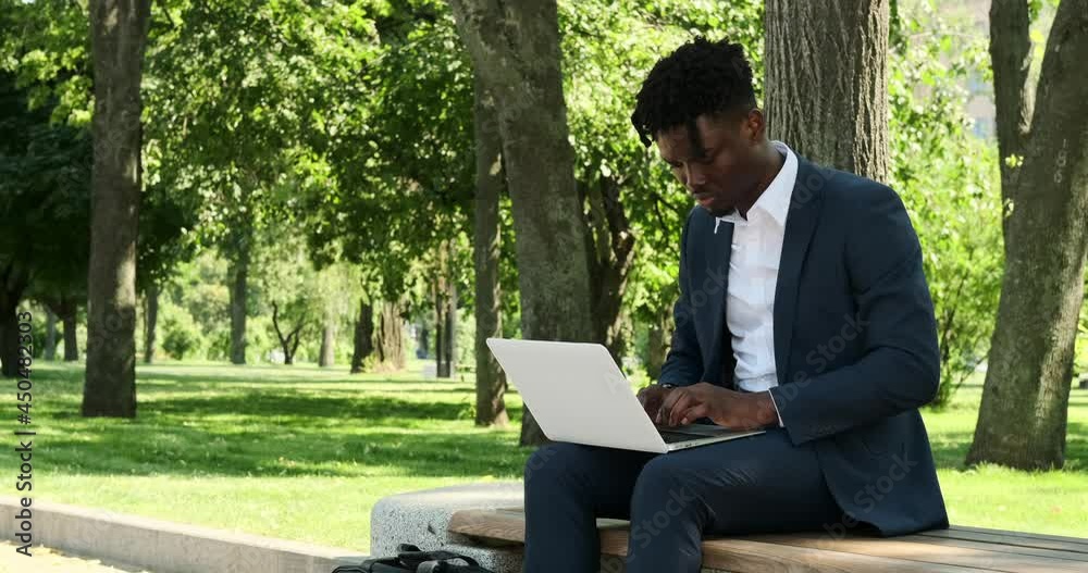African american businessman working on laptop outdoors at city park African american businessman working on laptop outdoors at city park