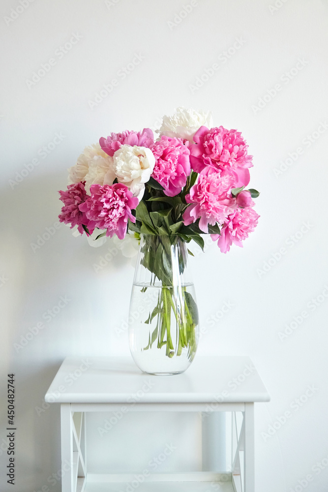 Fototapeta premium Empty white wall with pink flowers. Peonies in a glass vase in a bright interior