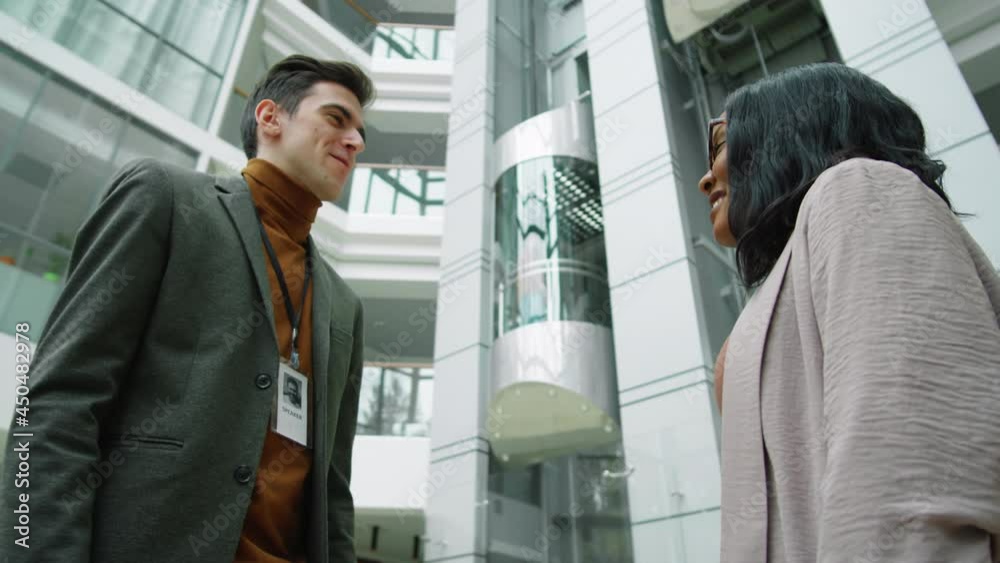 Low angle shot of young Caucasian businessman and Afro-American businesswoman shaking hands and speaking in modern office center Low angle shot of young Caucasian businessman and Afro-American businesswoman shaking hands and speaking in modern office center