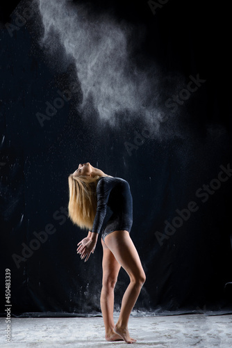 Beautiful blonde girl wearing a black gymnastic bodysuit covered with clouds of the flying powder